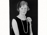 Kvinnoporträtt. Signe Beckman, Varberg iklädd ärmlös klänning med långt pärlhalsband och en dekoration fäst vid vänster axel.