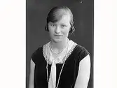 Porträtt av ung kvinna. Agnes Andersson från Lidarna Hunnestad, klädd i ärmlös klänning som har både spetskrage och slips. Långt pärlhalsband.