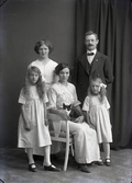 Familjebild, troligen makar med tre döttrar. Den äldre flickan i mitten sitter med en katt i knät. Beställare: John Olsson, sannolikt mannen på bilden.
