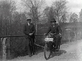 Två män på en grusväg. Mannen som sitter i hatt på motorcykeln, med stödet nedfällt, är Gösta Karlsson i Våghult, Krogsered.