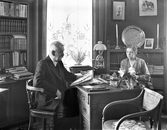 Borgmästare Johan H Linnemann Janssen sitter vid skrivbordet med en tidning och frun Annie i hörnrummet mot korsningen Kungsgatan-Eskilsgatan. Bostaden låg i 