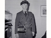 Porträtt av (buss?)chaufför Hugo Cederlund från Frillesås i sin yrkesuniform. Han bär en kassaväska där mynten förvarades i rören på utsidan.