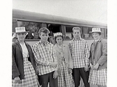 Fem ungdomar som är klädda i matchande rutiga skjortor och kjolar framför en buss. Flickorna har även rutiga, platta hattar.

Karl Fredrik Olsson var redaktör (ca 1935-1965) på Hallandsposten så bilden har troligen varit publicerad i tidningen.