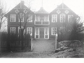 Folkets hus i Varberg kallat Lilla Kari. Tomten hägnas med ett trästaket vars öppning utan grindar är mitt för byggnadens entréparti.