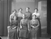 Ateljébild med sju unga kvinnor klädda i blusar och fotsida kjolar.