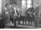 Realskolans mässingssextett poserar på en låg estrad med sina blåsinstrument tillsammans med en pianist och dirigent.
