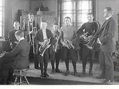 Realskolans mässingssextett poserar på en låg estrad med sina blåsinstrument tillsammans med en pianist och dirigent.