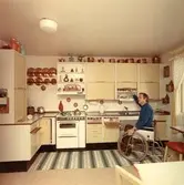 Man i rullstol visar handikappanpassat kök i Brickebacken, 1971