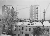 Rivningshus framför byggkranar över nybyggnation av hyreshus vid Drottninggatan, 1960-1961