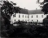 Troligen delar av familjen Carlheim-Gyllensköld utanför sitt gods, Vallens slott/säteri i Våxtorp. Byggnaden är vid fototiden ca 100 år; den uppfördes efter att den äldre brann ner år 1801. Byggherre var då hovjägmästare O W Burenskiöld. Delar av den medeltida borgen på platsen finns dock troligen kvar i bottenvåningen. Godset ligger på en holme i Vallsjön och med sitt läge i gränstrakterna Danmark-Sverige har många strider utkämpets här i raken. Vallen kom in i släkten Carlheim-Gyllenskiöld genom giftermål år 1830. Slottet med parkområde avstyckades 1939 från övriga markegendomar.