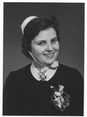 Bröstbild av Britt-Inger Johannesson, klädd i högtidsdräkt i samband med sjuksköterskeexamen vid Jönköpings läns landstings sjuksköterskeskola i december 1958.

Text på fotografiets baksida: 