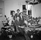 En medelålders man omgiven av sin familj samt korgar med gratulations blommor