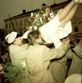 Kvinlig student blir kastad i luften av andra studenter