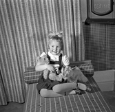 Familjen Hilda Ström, liten flicka sittandes på sängen med leksaker