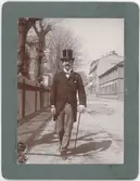 En man i hög hatt och käpp promenerar på Trädgårdsgatan, Uppsala