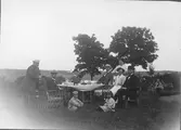 Sommarbild från Tofta. Personerna är samlade kring ett dukat trädgårdsbord. Resande handlande Sten Lidén, köpman Ernst Rylander, skräddarmästare Knut Svensson, Oscar Pehrson, Ellen Pehrson, Ingrid och handlande Hjalmar Sjöberg. Sitter På gräsmattan sitter barnen Håkan och Greta Perhrson.