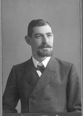 Ateljéfoto av specerihandlare Oscar Pehrson som bär delat hakskägg och mustach. Han är klädd i skjorta och dubbelknäppt kavaj. Hans affär låg i hörnet Kungsgatan-Norrgatan och kallades OP:s.
