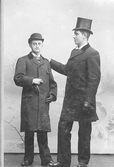 Mansporträtt av två herrar klädda i hatt och rock. Mannen till höger i hög hatt är handlanden Oscar Pehrson.