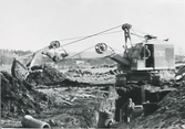 Två män utför rörläggningsarbete med hjälp av en grävmaskin på Ullas Lyckas väg, cirka 1970-tal.