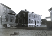 Ur byggmästare Johannes Nilssons fotoalbum från 1914. Gatumiljö med bostadshus i kv Falkenbäck, Borgmästaregatan 35-37. Huset till vänster har luckan till källaren öppen. På hörnan tilll höger ligger Carl Löebs Bleck & plåtslageri med verkstad in på gården.