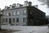 Ur byggmästare Johannes Nilssons fotoalbum från 1914. Huset på Kyrkogatan 33 i hörnet vid Östra Vallgatan, som går på höger sida. Till vänster skymtar byggmästarens eget hus uppfört 1896. Till skillnad från den artikulerade fasaden på hans bostad har denna byggnad en stram tegelfasad med endast en tandsnittsdekor under takfoten. På det avfasade hörnet sitter en balkong och taket har fem takkupor med stora fönster. I porten står ett barn och vid trappan nedanför står en pojke med en kärra.