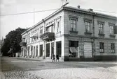 Ur byggmästare Johannes Nilssons fotoalbum från 1914. Fastigheten på Kungsgatan 18-Borgmästaregatan 8 i kv Prosten. Här stod tidigare en byggnad från 1700-talets mitt uppfört av Jacob Lagerbom. Eftersom släkten Reenstierna ägde fastigheten några decennier under 1800-talets första hälft kallas byggnaden Reenstiernas hus. Efter en brand 1889 fick huset detta utseende, då ägt av kronolänsman Emil Andersson. 

Ett skyltfönster vid Borgmästaregatan täcks av en skylt med reklam för Aug. Schüllerquists Manufakturlager med klädeshandel, damskrädderi, damkappor, herrekiperingsaffär, sybehör, mattor och gardiner.