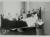 Sjukvård. Kyrkoherde Möller på lasarettet med ett par sjuksköterskor vid sängen.