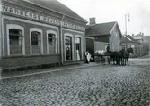 Ur byggmästare Johannes Nilssons fotoalbum från 1914. Warbergs mejeri AB på Prästgatan 26 i kv Guldsmeden. Byggnaden uppfördes 1883 men Nilsson var involverad i en ombyggnad 1911. Mejeripersonal står vid entrén vid ett hästekipage med vagnen full av mjölkkannor. 