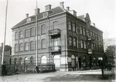 Ur byggmästare Johannes Nilssons fotoalbum från 1914. Affärs- och bostadsbyggnad i Falkenberg uppförd i tegel 1905 på Storgatan 45 i kv Lönnen, sett från Hallanäsgatan. Fasaden har både horisontal och vertikal mönsterdekor, där den senare omges av putsade, försänkta ytor. Balkongernas buktande smidesräcken var en typ Nilsson använde på flera hus vid tiden. På bottenplan ligger både en pappershandel och Kooperativa Handelsföreningen. På taket i bakgrunden ses en telegrafanordning.