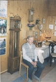 Paul Eriksson, Heljered, sitter på en stol i Missionskyrkan, cirka 1990. Troligtvis är det vid en hantverksutställning. Väggarna i bakgrunden är klädda med träpanel.