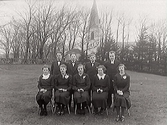 Liten konfirmandgrupp utomhus i Skällinge år 1938 med prästen till höger och kyrkan i bakgrunden.