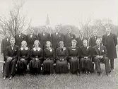 Konfirmander i skällinge med prästen Söhrman till höger och kyrkan i bakgrunden.