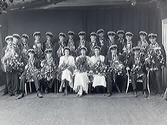 Realexamen 1932. Stor grupp studenter med tre flickor och resten pojkar i studentmössor och dekorerade med blomsterbuketter.