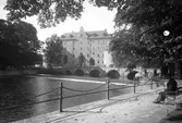 En man sitter på en parkbänk i skuggan i Centralparken, mot Örebro slott och kanslibron, 1930-tal