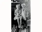 De två döttrarna till Anny och Victor Daniel Elofsson i Vinberg i likadana klänningar och skor intill en byrå.