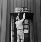 Vaktmästare Körberg sätter upp skylten vid Wadköpings diversehandel, Wadköpings handelsbod i Tenngjutaregården, kulturreservatet Wadköping.