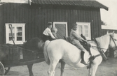 Sittandes på den vita hästen är Roland Svensson, Backen eller Högen (nedre gården), början av 1900-talet. Roland var son till Klara, som var väninna med Matilda Pettersson. Han var fosterbarn hos Birger Pettersons mor Augusta Pettersson (1863 - 1943). Huset i bakgrunden är magasin/uthus till nedre gåren. Den var även sommarbostad. Barnen i bakgrunden saknar namnuppgifter.