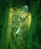 Resande Man. Lodfoto med metallföremål 53 mitt i bild mellan två däcksbalkar. Notera läderstycket höger om, samt blocket och bronshjulet ovanför, metallföremålet.