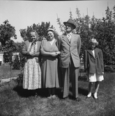 Ernst och Evelina Larsson i Utmossen, Fageråkra, med dottern Irma till höger och Bertha i Nykvarn till vänster. De står finklädda i trädgården och till vänster i bild står en rad bikupor i bakgrunden. (Se även EA0390, EA0389)
