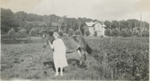 Ingeborg Gustafsson (1901 - 1987, gift Johansson) står på ängarna hållandes en arbetshäst, okänt årtal. I bakgrunden ses Gamla Riksvägen samt föräldragården Kållered Stom 