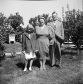 Ernst och Evelina Larsson med dottern Irma i trädgården på Utmossen, Fageråkra med bikupor i bakgrunden. (Se även bildnr EA0388, EA0390)