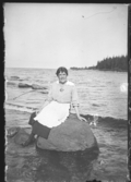 En kvinna sitter på en sten i vattnet.