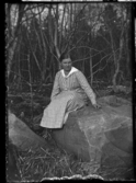 En kvinna sitter på en sten, klädd i rutig klänning.