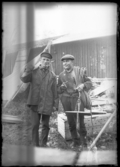 Två män med pipor i händerna bärande på verktyg och rep.