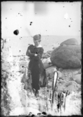 En kvinna i klänning på stenig strand.