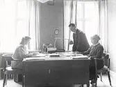 Varbergs Erkända Sjukkassa. Syster Ellen Johansson, Gunnar Benson och Rut Henriksson kring skrivbordet. Kontoret låg på Torggatan 26 i  kv Sadelmakaren.