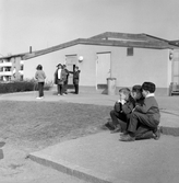 Flickor med hopprep och pojkar som vilar på Södra Lillåstrandskolans skolgård, 1960-tal