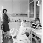 Barnen dricker saft medan fru Enbrant diskar i köket i Baronbackarna, 1960-tal