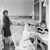 Barnen dricker saft medan fru Enbrant diskar i köket i Baronbackarna, 1960-tal
