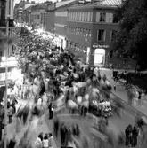 Vissa marknadsbesökare står still medan de flesta rör sig på marknadsafton, juni 1972